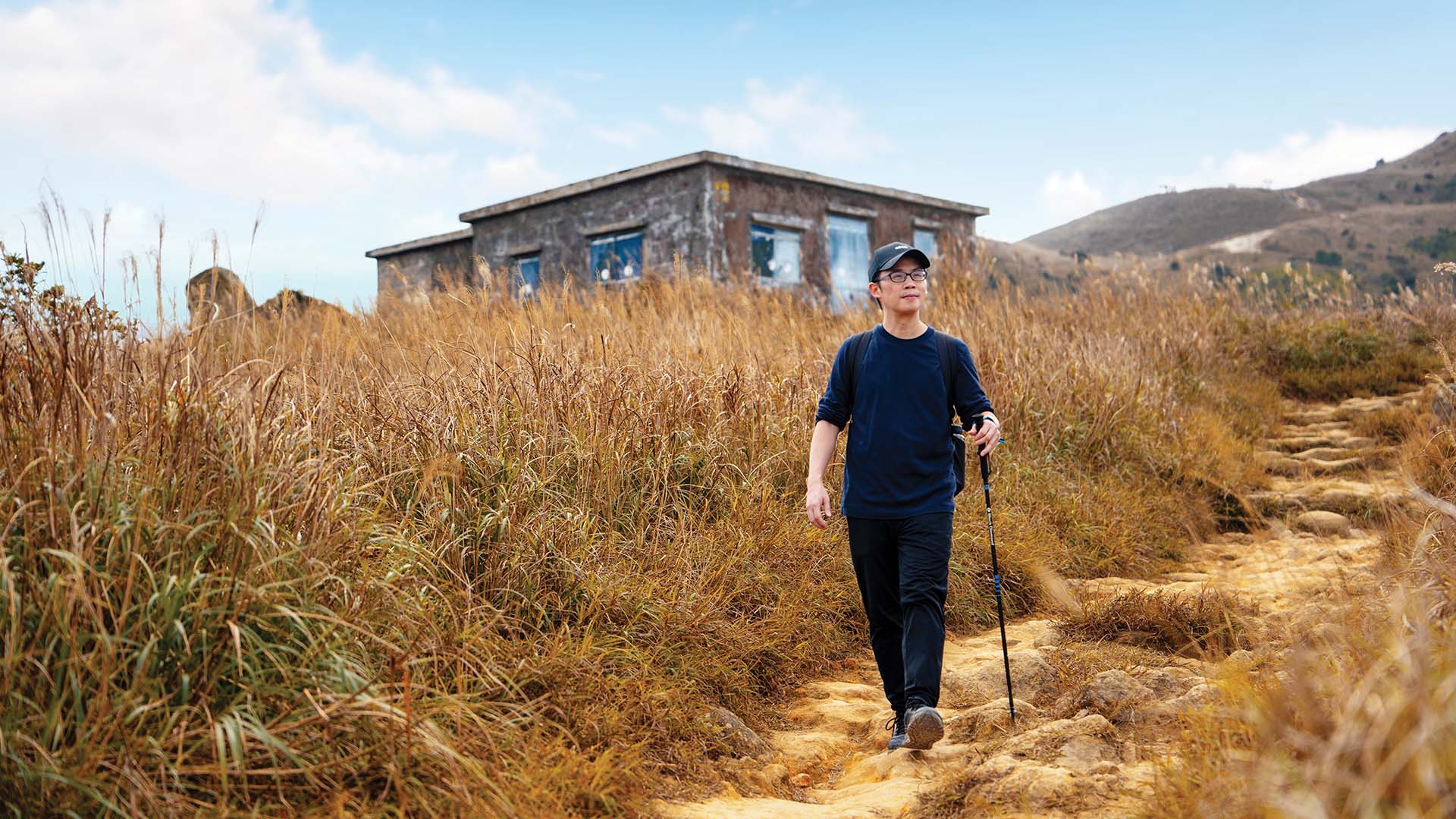 Thomas Chung hiking at Lantau Mountain Camp, surrounded by Chinese Silvergrass and stone cabins