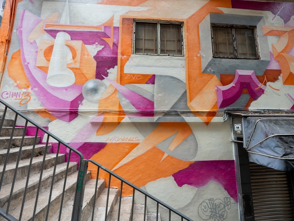 A wall painted with a pink, orange and grey mural by Chan13 on Square Street. 