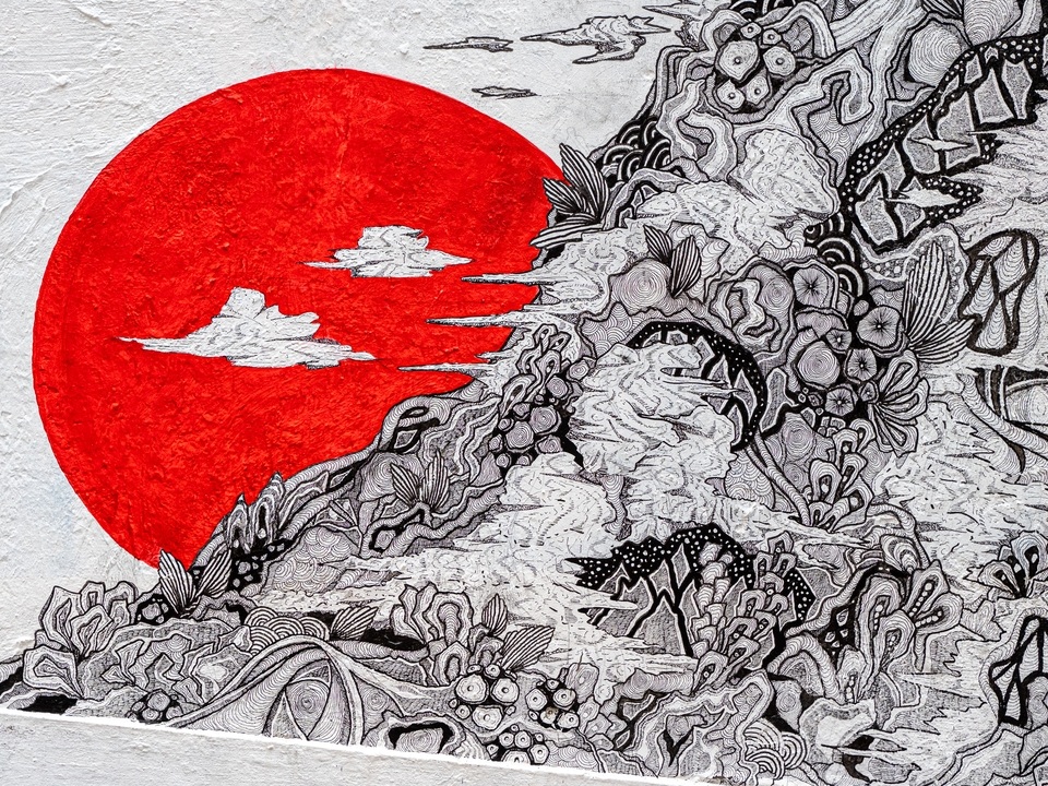 Close up of a red sun behind black and white lines depicting nature on an mural by Joe Ellul. 