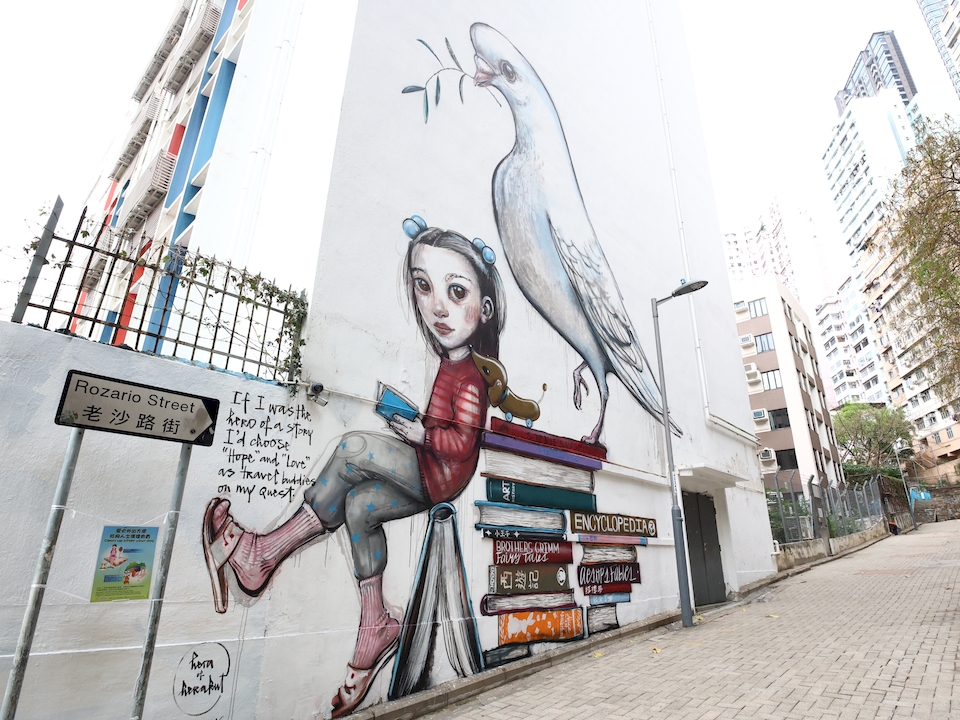 Large mural of a white bird and a girl amid two stacks of books by Hera on Rozario Street. 