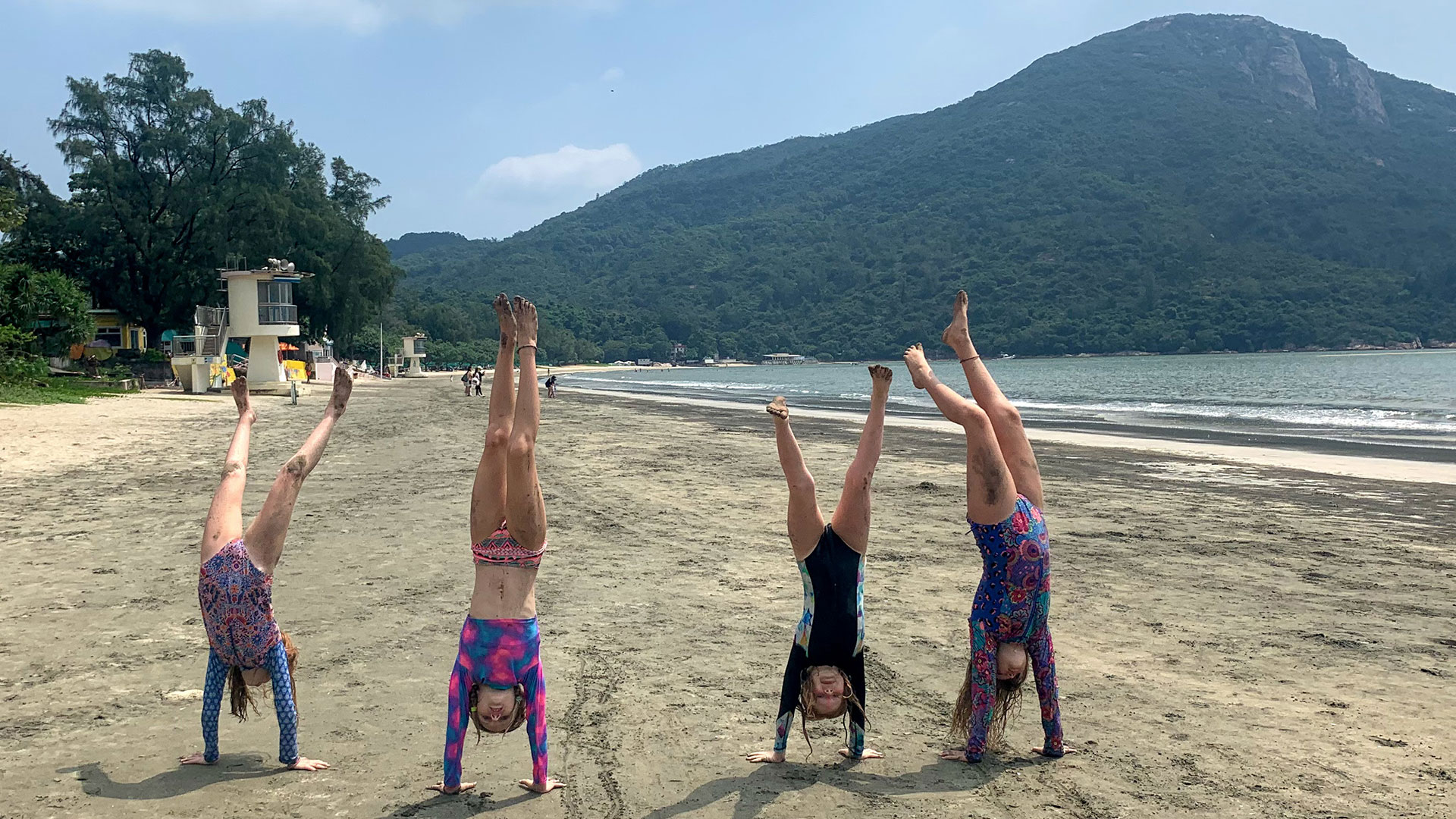 Four people do hand-stands on a beach